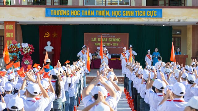 A vibrant school ceremony in Vietnam featuring students in white uniforms and hats waving flags.