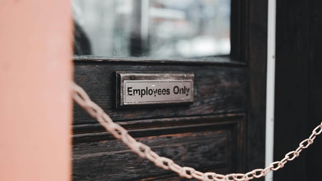 Close-up of an 'Employees Only' sign on a rustic wooden door secured by a chain.