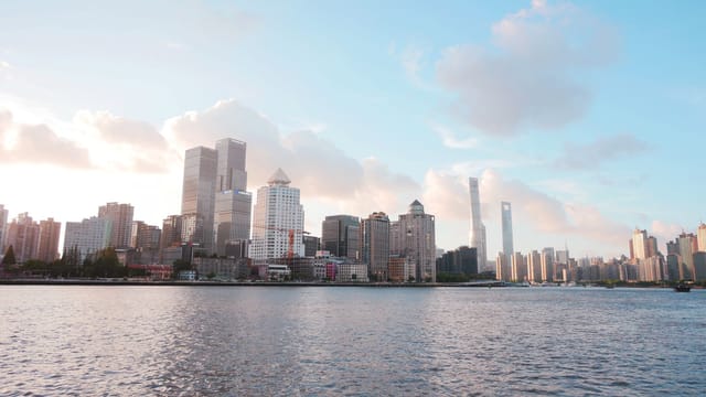 Skyline of Shanghai with modern skyscrapers under a bright sky and river view.