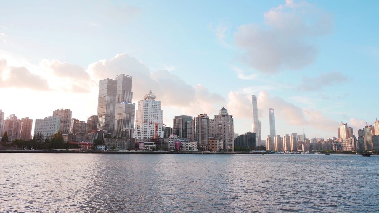 Skyline of Shanghai with modern skyscrapers under a bright sky and river view.