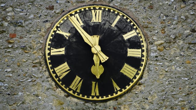 Close-up of a vintage clock face with Roman numerals on an exterior wall.