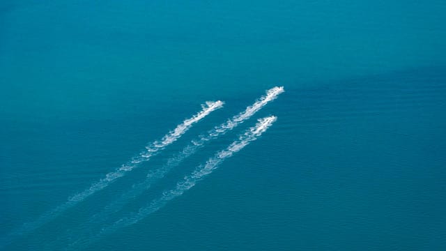 Aerial shot of two speedboats leaving trails on a vast turquoise sea, creating dynamic white wakes.