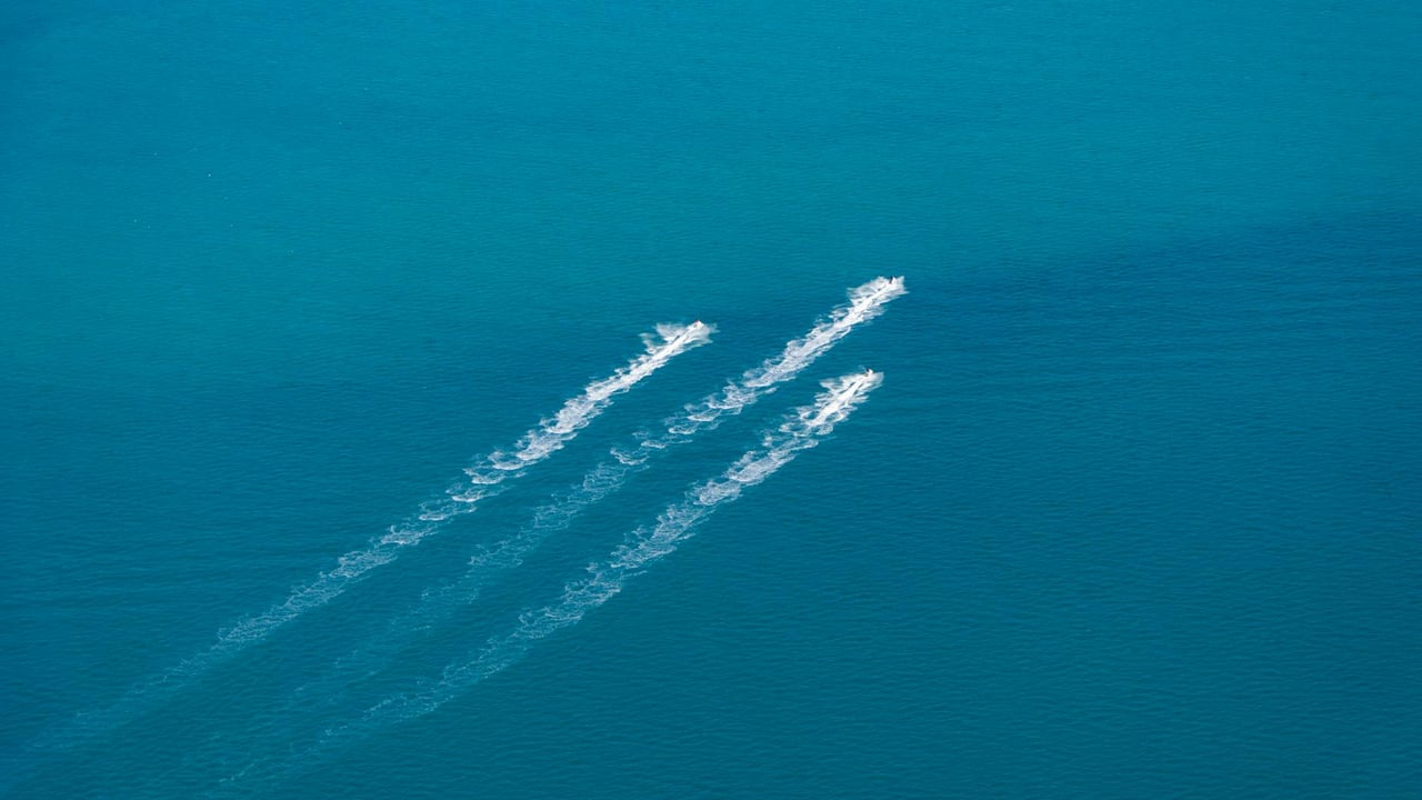 Aerial shot of two speedboats leaving trails on a vast turquoise sea, creating dynamic white wakes.