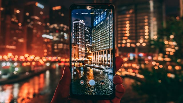 A smartphone capturing the illuminated Chicago skyline at night with Trump Tower in focus.