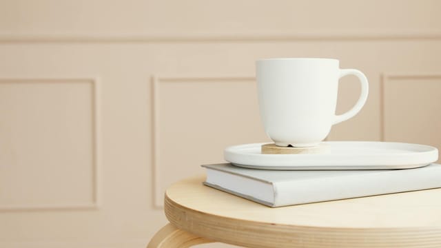 A white ceramic mug on a tray, placed over a closed book on a wooden table.
