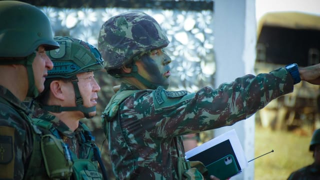 Soldiers in camouflage and helmets strategizing outdoors, focusing on a mission directive.