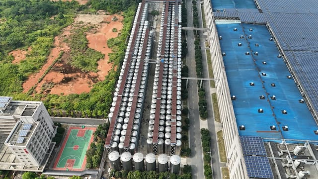 Aerial shot of a factory with solar panels and silos in a green landscape.
