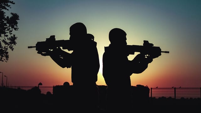 Silhouette of two soldiers with rifles against a vivid sunset sky, creating a dramatic scene.