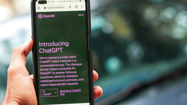 Close-up of a smartphone showing ChatGPT details on the OpenAI website, held by a person.