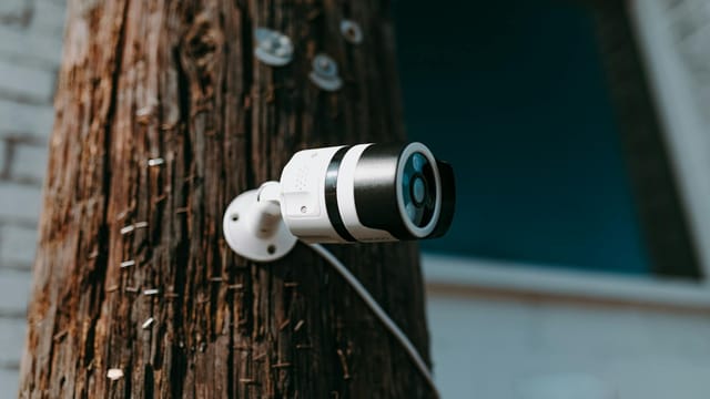 Close-up of a modern security camera mounted on a wooden post outdoors.