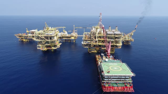 Aerial shot of multiple offshore oil platforms in a serene, blue sea under clear skies.