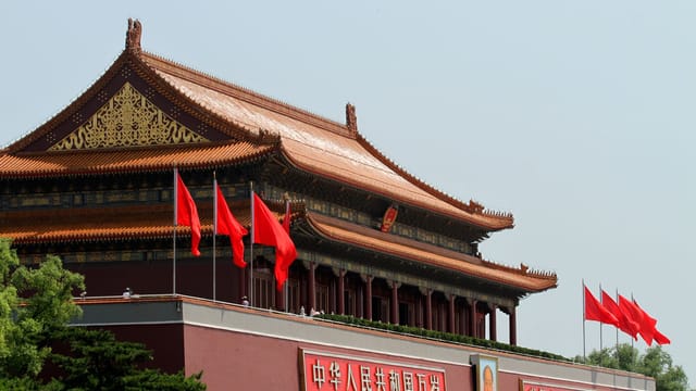 Tiananmen Gate in Beijing, China with vibrant red flags under a clear sky.