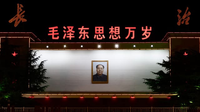 Night scene showing a portrait of Mao Zedong on an illuminated Chinese wall, emphasizing political history.