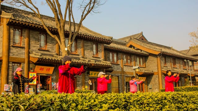 Women practicing Tai Chi in a traditional Chinese street near a temple during the day.
