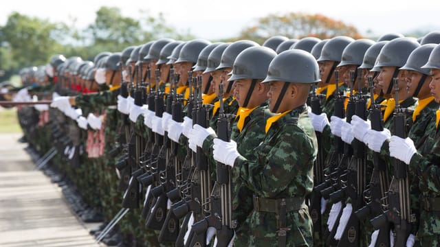 Side view Asian military troop in khaki uniform including white gloves and helmets marching with rifles in army