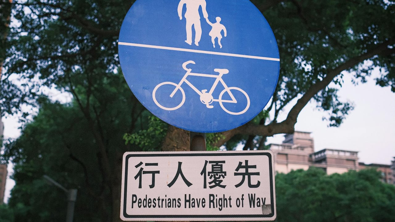 Sign indicating pedestrian right of way with bicycle path in a leafy urban park.
