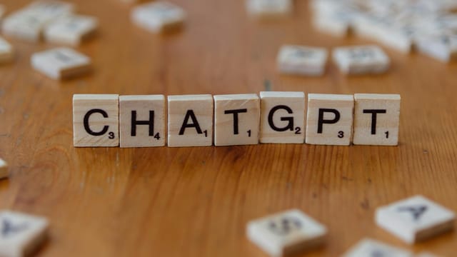 Scrabble tiles spelling "CHATGPT" on wooden surface, emphasizing AI language models.