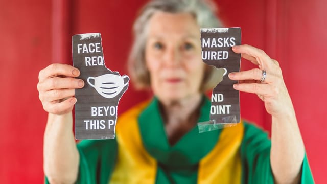 Senior woman holding torn COVID mask requirement sign symbolizing protest.