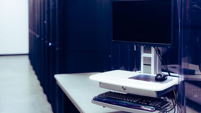 Illustrative image: Contemporary computer with black screen placed on stand near row of server steel racks in data center