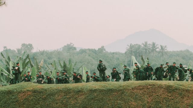 A group of soldiers in green uniforms march through lush jungle terrain, showcasing military training.