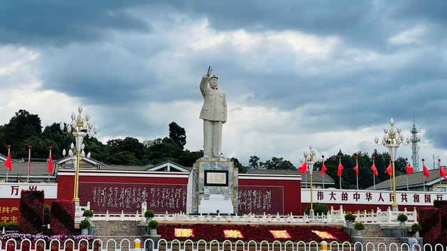 Statue of Mao Zedong in a public plaza with red flags and Chinese inscriptions.