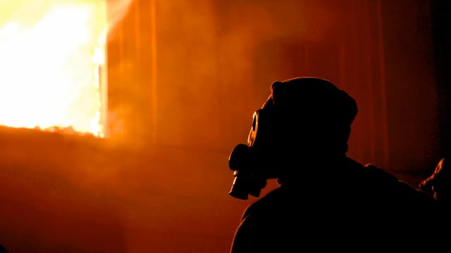 Eerie silhouette of a person with a gas mask in profile, facing intense flames and smoke.