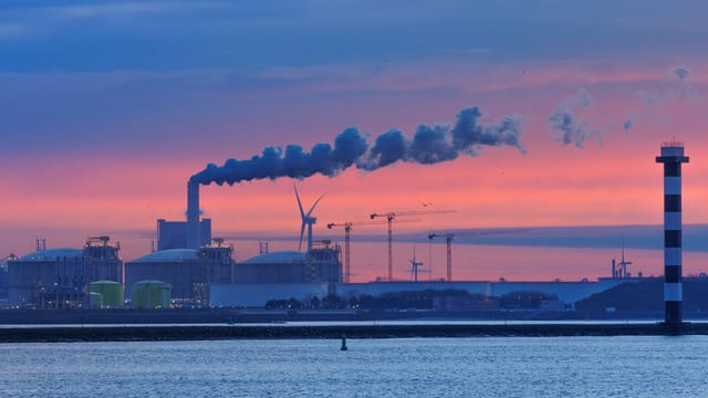 Smoke from a factory chimney at sunset in Hook of Holland, Netherlands, illustrating industrial impacts on the environment.