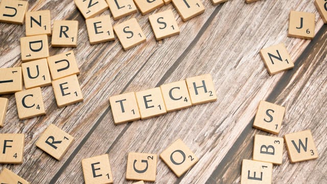 Wooden Scrabble tiles spelling 'TECH' on a textured surface, showcasing creativity.