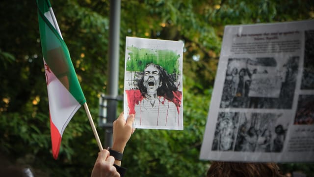 Protesters in Stockholm hold signs and an Iranian flag during a demonstration for social change.