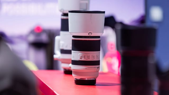 A detailed shot of a professional telephoto camera lens on a red table, with a blurred background.