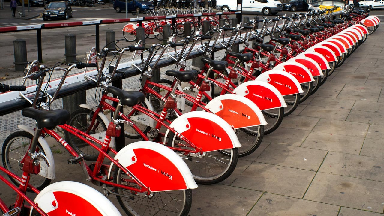 A long row of red rental bicycles parked in Barcelona city street.