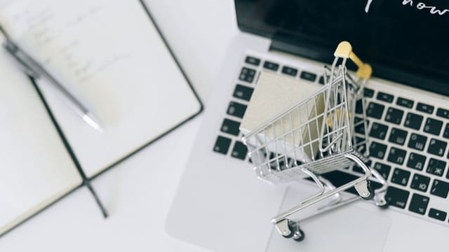 Creative depiction of online shopping with a miniature cart on a laptop keyboard.