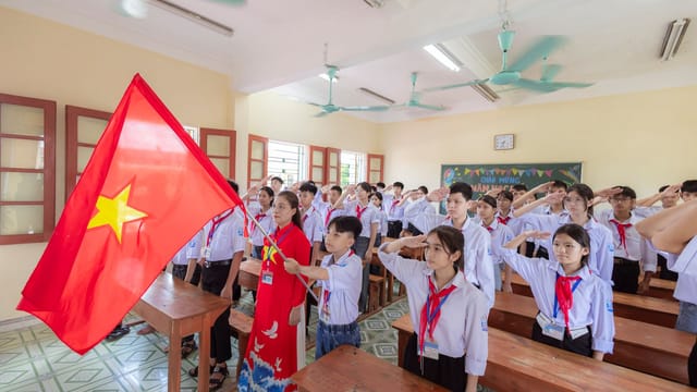 Students in uniform saluting with national flag in a classroom setting during the day.