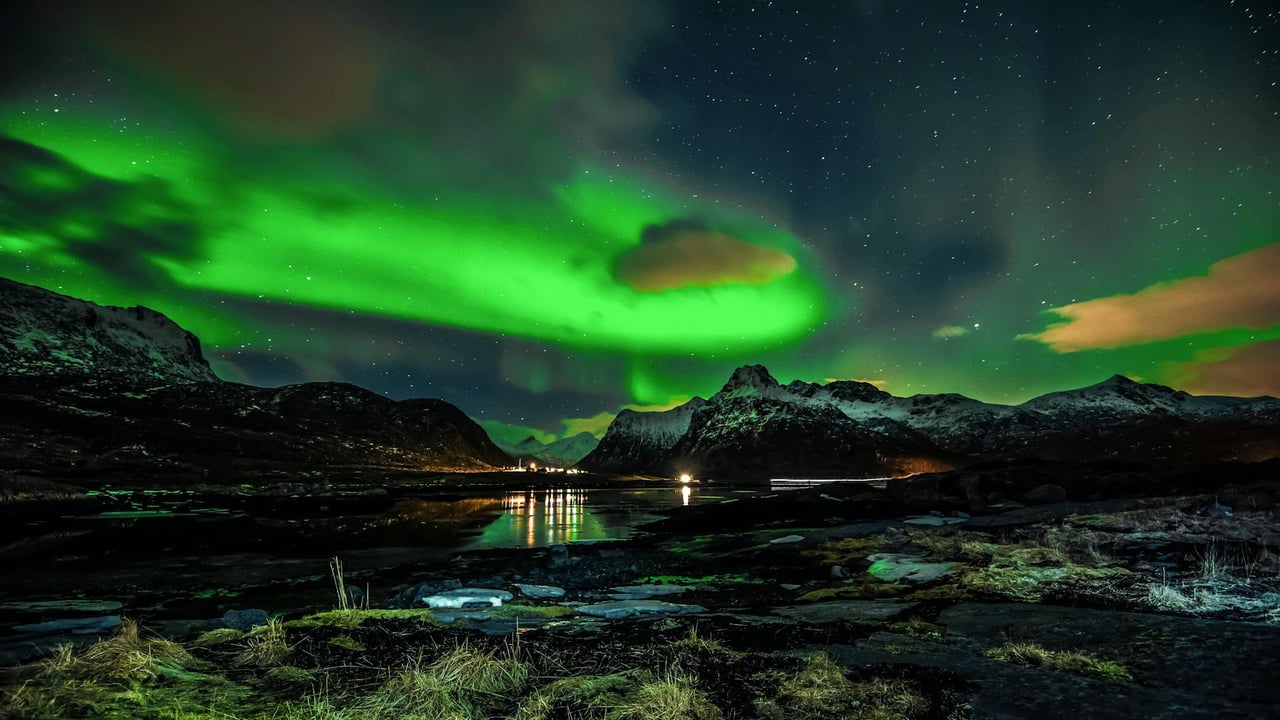 Vibrant aurora borealis illuminating the night sky over a serene mountain and lake landscape.