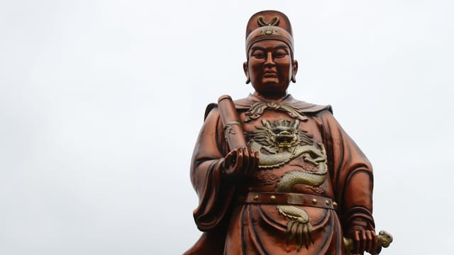 A low-angle view of the Zheng He statue at Sam Poo Kong in Semarang, Indonesia, under a white sky.