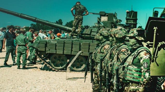 Group of camouflaged soldiers near a tank during a training exercise outdoors.