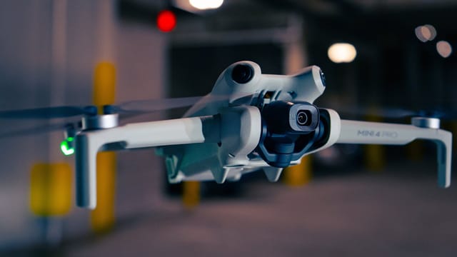 A close-up shot of a quadcopter drone hovering in an indoor setting.