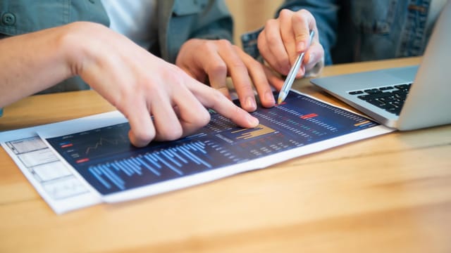 Collaborative discussion over data charts and laptop, focusing on business strategies.