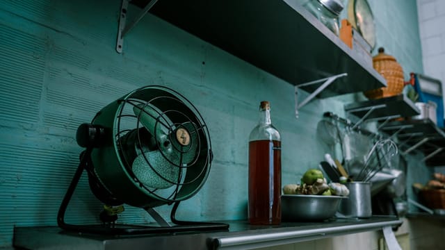 A rustic kitchen scene featuring a vintage fan, cookware, and open shelves, evoking a retro Brazilian style.