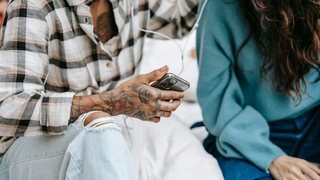 Crop unrecognizable diverse friends in casual clothes sitting and listening to music in earphones in daytime