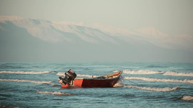 A solitary boat floats on the waves of the Caspian Sea with mountain views in Gorgan, Iran.