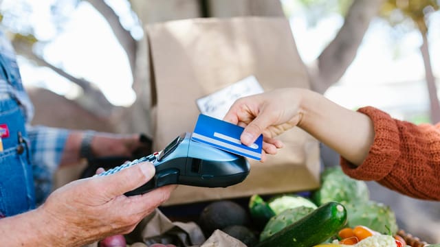 A customer making a contactless payment with a credit card at a farmers market.
