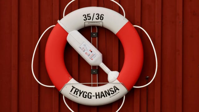 A lifebuoy with rope for emergencies mounted on a red wall, featuring Trygg-Hansa branding.