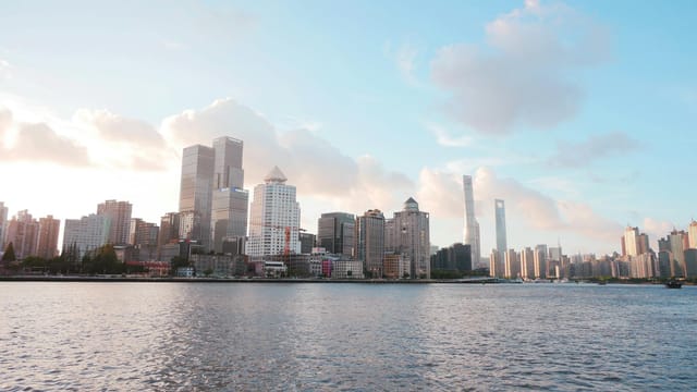 Skyline of Shanghai with modern skyscrapers under a bright sky and river view.