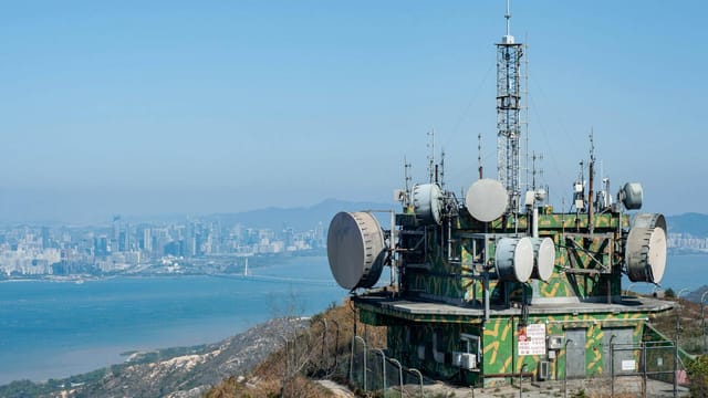 A telecommunications tower on a hill overlooking the Hong Kong city skyline and water.