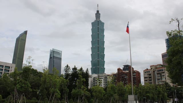 Skyline view of Taipei 101 with cityscape and Taiwanese flag on a cloudy day.