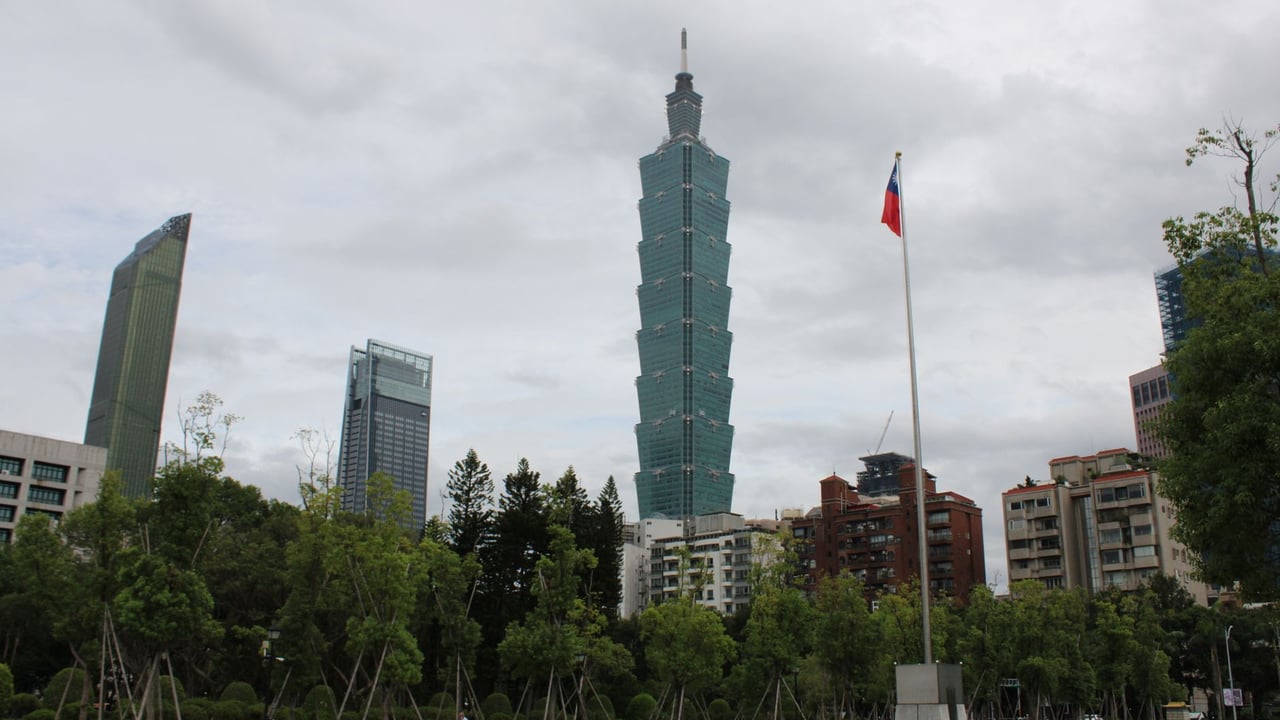 Skyline view of Taipei 101 with cityscape and Taiwanese flag on a cloudy day.