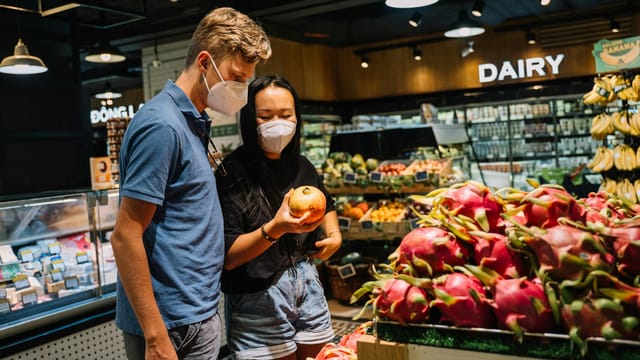 A couple wearing face masks shopping for fresh fruits at an indoor supermarket.