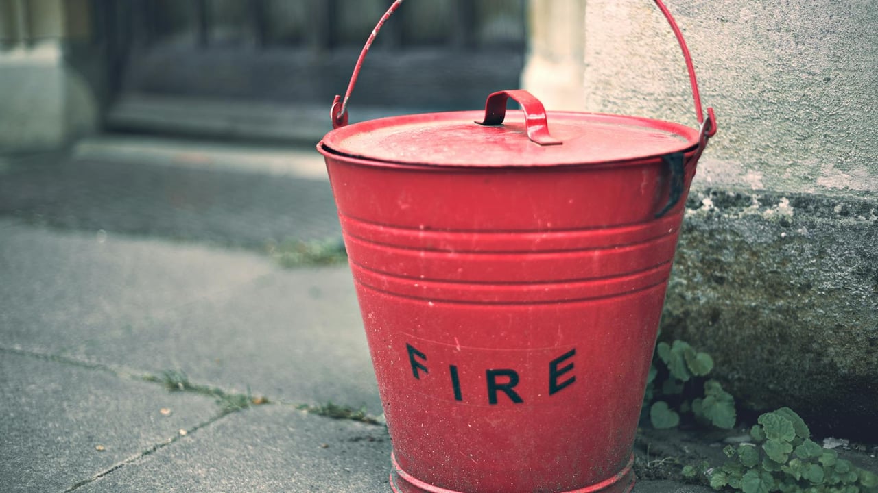 Rustic red fire bucket on a stone surface, evoking vintage charm and nostalgia.