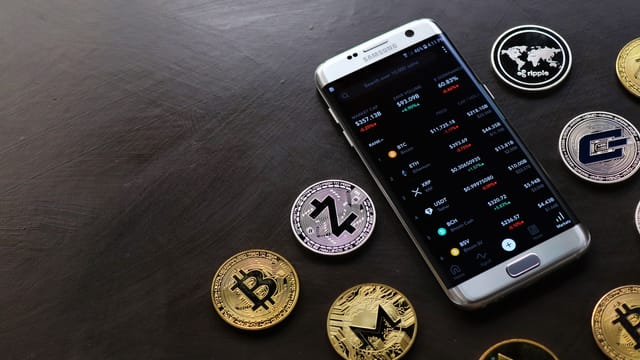 A collection of cryptocurrency coins and a smartphone displaying a digital trading platform.